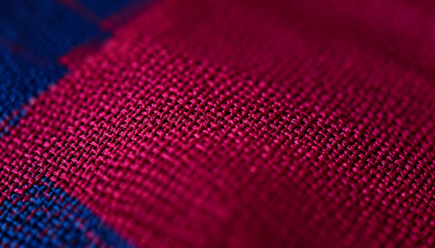 Extreme close-up photograph of ripstop nylon fabric in deep crimson red, showing the fine crosshatch weave texture and subtle sheen under soft diffused light