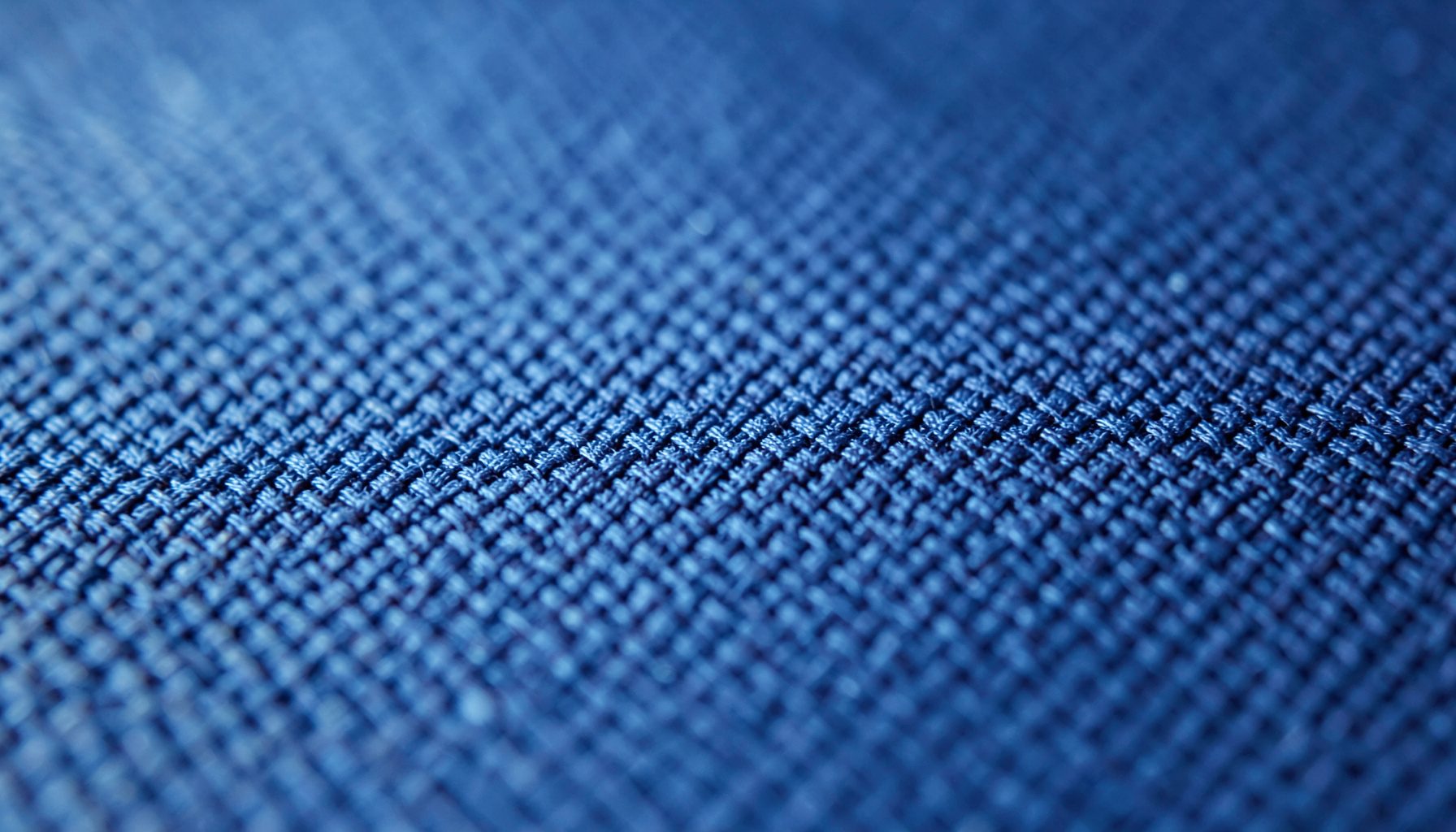 Close-up of ripstop nylon fabric texture with subtle crisscross grid pattern, deep navy blue tones fading into lighter sky-blue highlights, soft diffused lighting revealing the material's fine weave