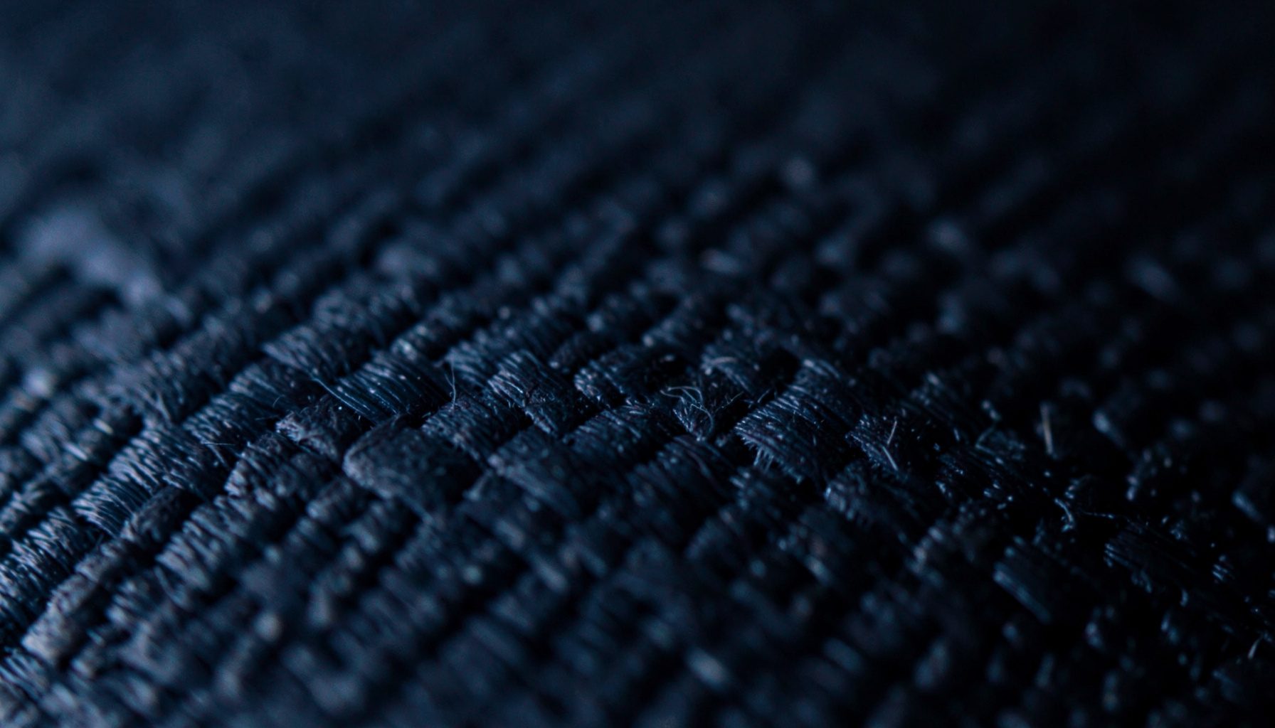Extreme close-up photograph of a carbon-fiber composite surface in deep charcoal black with subtle diagonal weave lines catching the light